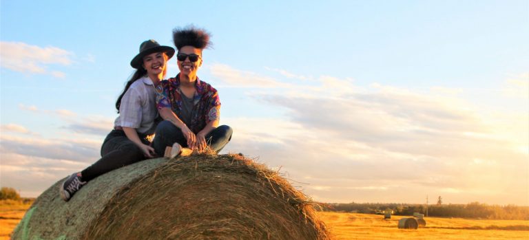 Two females sitting atop a hay bale with golden sunlight falling on them