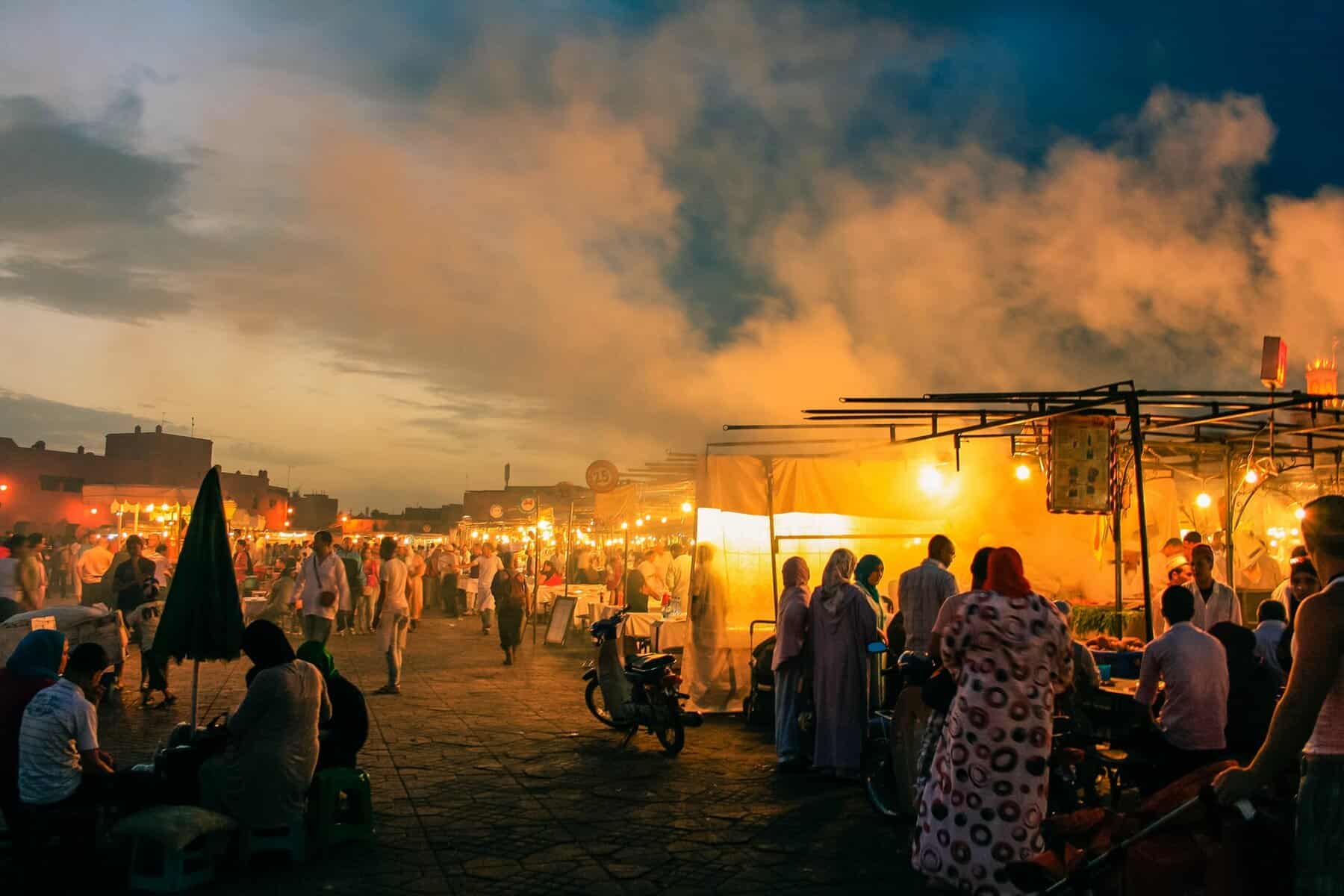 Busy market with stalls and people in the sunset in Marrakech