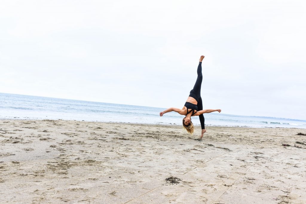 Woman in black outfit doing a somersault on a beach