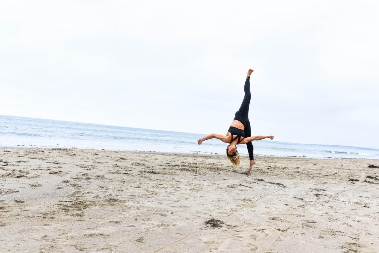 Woman in black outfit doing a somersault on a beach