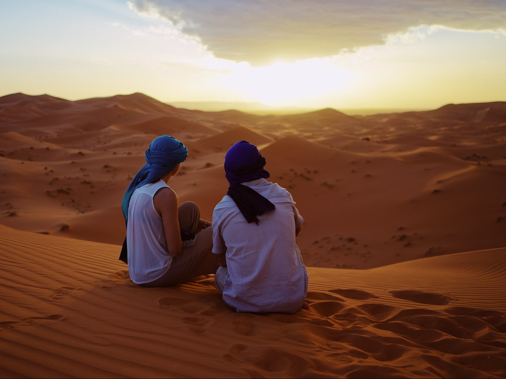 Man and woman with head gear looking at a sunset over a desert in Morocco.