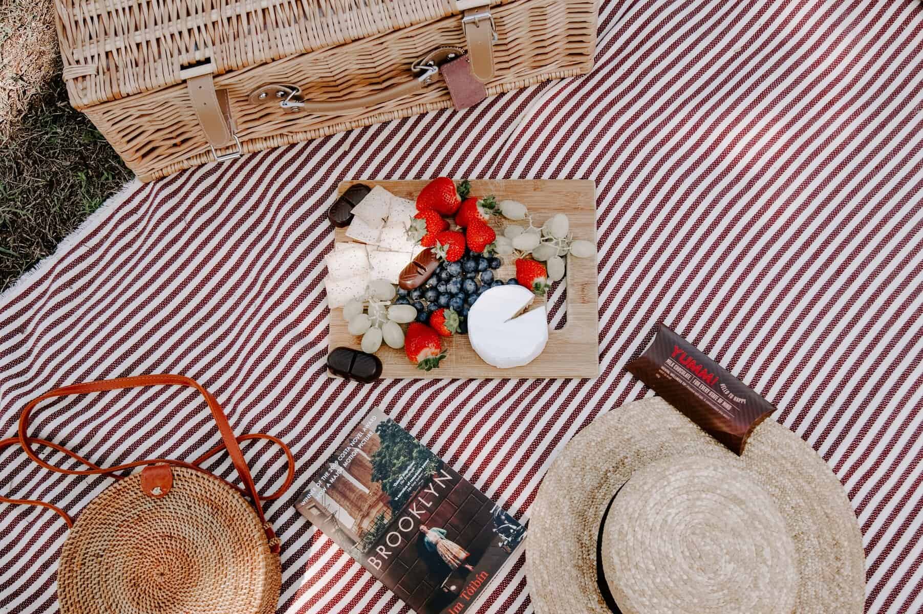 Picnic basket, book, hat and flowers laid out on a red and white cloth