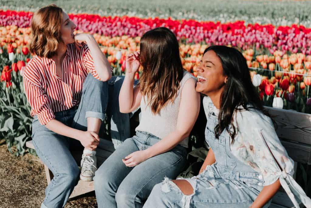 Three women sitting on a bench near flowers, laughing